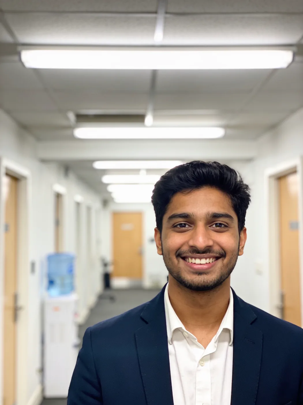 A man in a navy blazer photographed in an office corridor