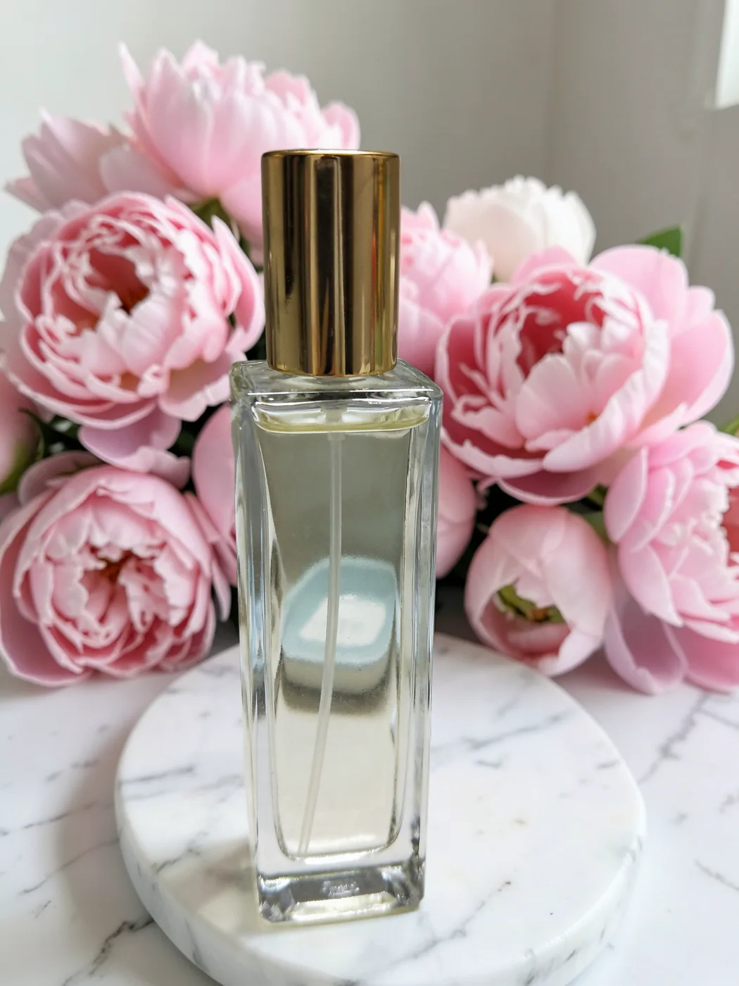 The same perfume bottle, unchanged, on a marble pedestal with pink peonies made by AI