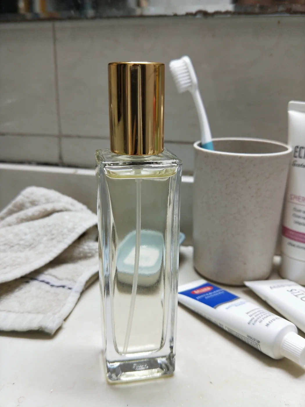 A glass perfume bottle on a cluttered bathroom counter